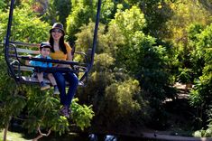 a woman and her son ride on a swing in the air over water, surrounded by trees