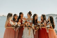 a group of women standing next to each other holding bouquets in front of the ocean