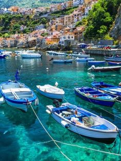 many small boats are tied up in the clear blue water near some buildings and cliffs