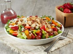 a white bowl filled with salad next to a wooden bowl full of strawberries and almonds