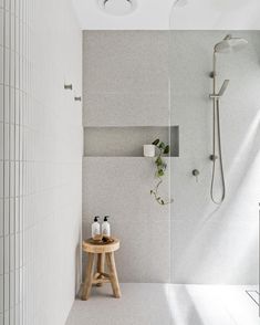 a white tiled bathroom with a wooden stool and shower head mounted to the wall next to it