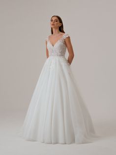 a woman wearing a white wedding dress with sheer neckline and open back, standing in front of a white background