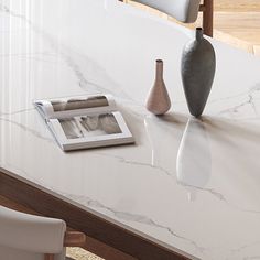 two vases sitting on top of a white marble table next to a magazine holder