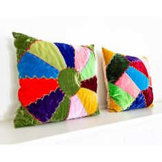 two colorful pillows sitting on top of a white shelf