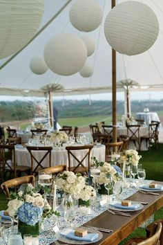 a table set up with plates and vases in front of white paper lanterns hanging from the ceiling