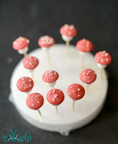 red and white cake pops sitting on top of a white frosted cake with sprinkles