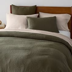 a bed with green comforter and pillows on top of it next to a night stand