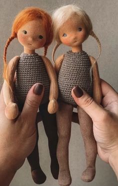 two little dolls sitting on top of each other in their hands, one being held by someone's hand