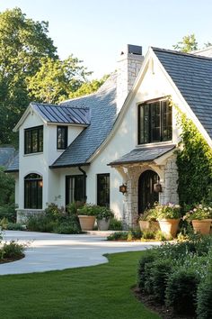 a large white house with lots of windows and plants in the front yard on a sunny day