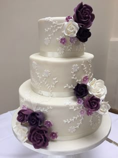 a three tiered wedding cake with purple and white flowers on the top, sitting on a table