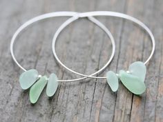 two silver hoop earrings with green sea glass flowers on each earring, sitting on a wooden surface