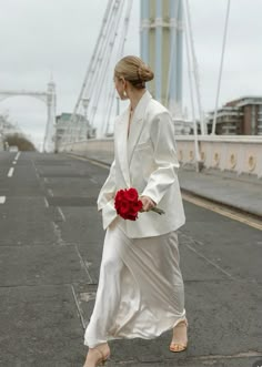 a woman is walking down the street with a flower in her hand while wearing a white suit