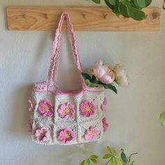 a crocheted purse hanging on a wall with flowers in the vase next to it