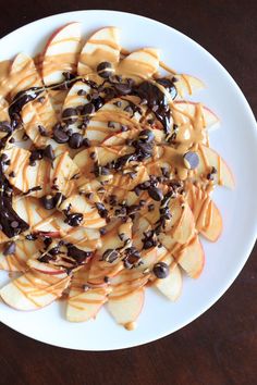 a white plate topped with sliced apple slices covered in chocolate chips and caramel sauce