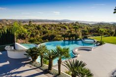 an outdoor swimming pool surrounded by palm trees and greenery with mountains in the background