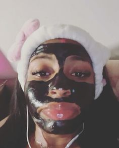 a woman with black face mask and bunny ears on her head wearing earphones, holding up a cell phone in front of her face