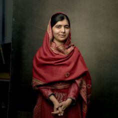 a woman wearing a red shawl standing in front of a black wall with her hands on her hips