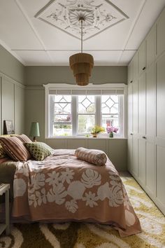 a bed sitting under a window in a bedroom next to a dresser and lamp on top of a rug