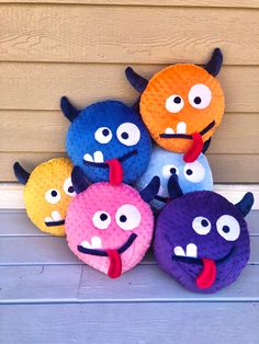 five different colored stuffed animals sitting on the ground next to a wall with eyes and mouths