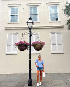 a woman standing next to a lamp post with flowers hanging from it's sides