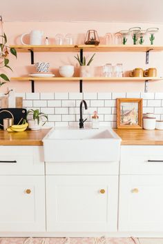 a white kitchen sink sitting under a window next to a shelf filled with pots and pans