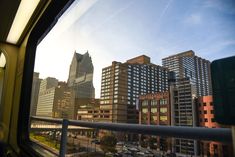 the view from inside a train looking at tall buildings in the distance and cars parked on the street