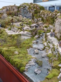 people are standing on the side of a hill next to a small river and bridge