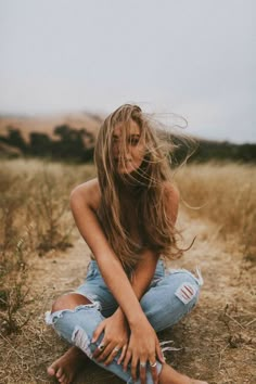 a woman sitting in the middle of a field with her hair blowing in the wind