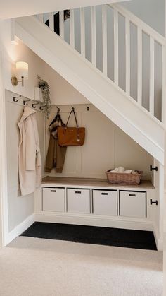 a coat rack under a stair case with white drawers and storage bins underneath it