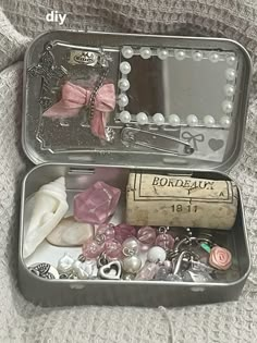 an open tin box filled with jewelry on top of a bed