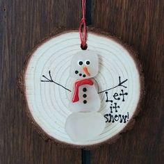 a snowman ornament hanging on a wood slice with the words let it snow