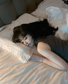 a woman laying on top of a white bed next to an unmade pillow and pillows