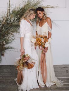 two beautiful women standing next to each other holding bouquets