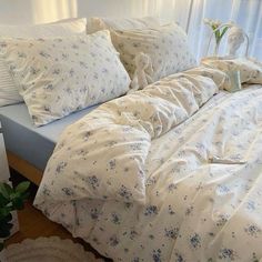 an unmade bed with white sheets and blue flowers on it in front of a window