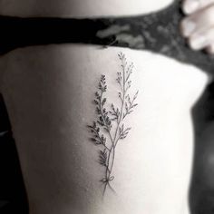 the back of a woman's stomach with a small plant tattoo on her side