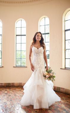 a woman in a wedding dress posing for a photo with windows behind her and flowers on the floor