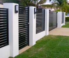 a row of black and white fences next to a green lawn with palm trees in the background