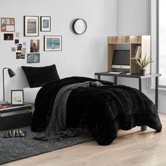 a bed with black comforter and pillows in a room next to a wall with pictures on it