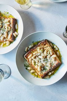 two white plates with food on them next to wine glasses