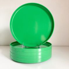 three green plates sitting on top of each other in front of a white wall,