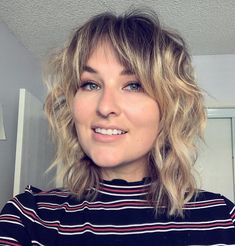 a close up of a person with blonde hair and blue eyes wearing a striped shirt