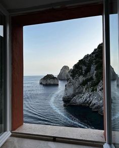 an open window looking out at the water and rocks in the ocean from inside a house