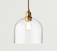 a clear glass pendant light hanging from a ceiling fixture with an antique brass metal finish