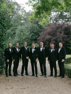 a group of men in tuxedos standing next to each other on a gravel road