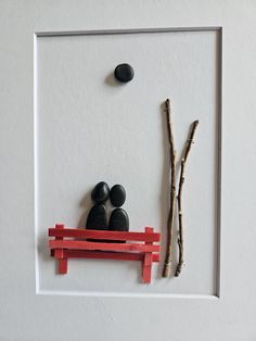 two black rocks sitting on top of a red bench next to a branch and rock