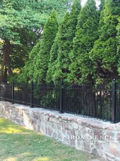 a stone wall with black iron fence surrounding it and trees in the backround