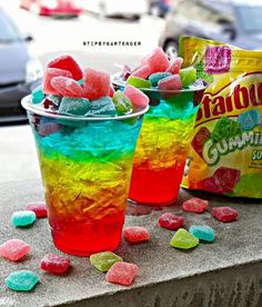 two cups filled with gummy bears sitting on top of a table next to a bag of candy