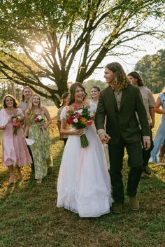 a bride and groom walking through a field with their bridal party in the background