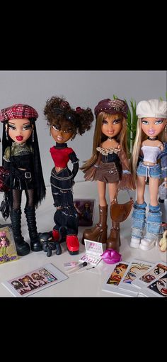 four dolls are standing next to each other on a table with cards and pictures around them