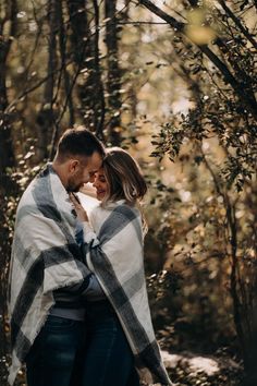 a man and woman standing in the woods under a blanket wrapped around each other's shoulders